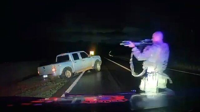Policiais em operação rodoviária apontam arma em direção a uma picape parada na lateral da rodovia BR-163 à noite