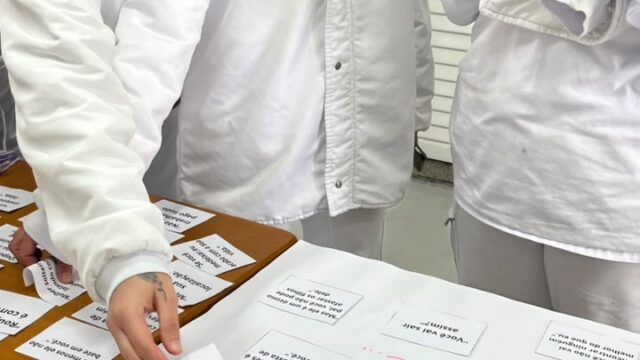 Três colaboradores de uniforme branco participam de dinâmica com cartazes sobre violência contra a mulher em Ponta Grossa