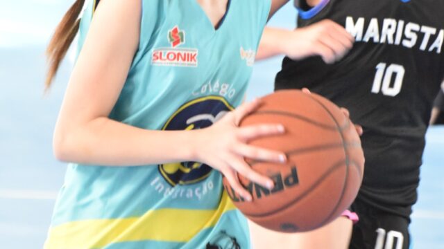 Duas jovens atletas disputam a bola em partida de basquete durante competição estudantil