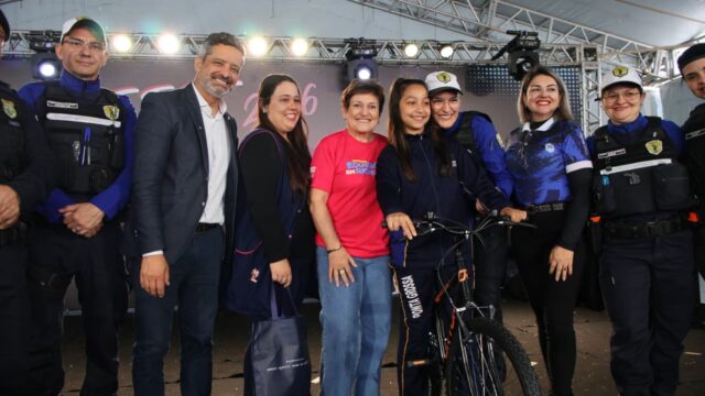 Estudante segura o guidão de uma bicicleta no palco ao lado de autoridades e educadores em Ponta Grossa