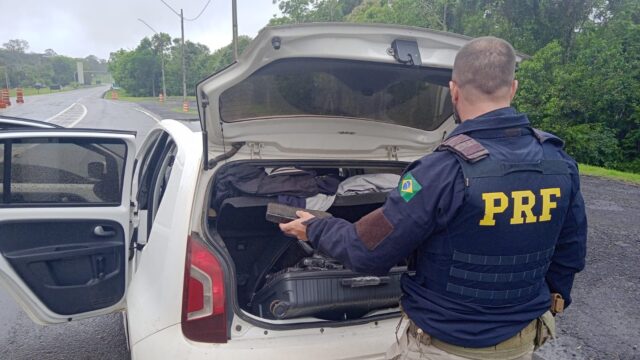 Policial da PRF vistoria porta-malas de carro branco com entorpecentes na BR-373