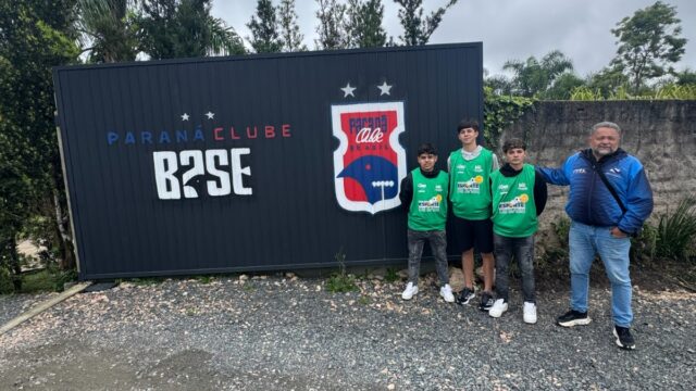 Três jovens atletas e um homem posam diante de um muro com a identificação do Paraná Clube em Curitiba