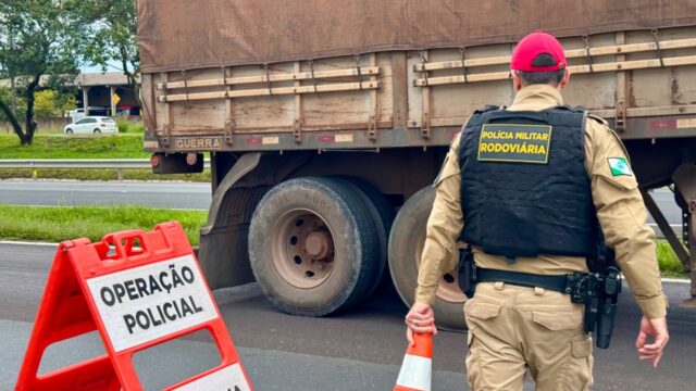 Policial militar rodoviário de costas em fiscalização de caminhão em rodovia no Paraná