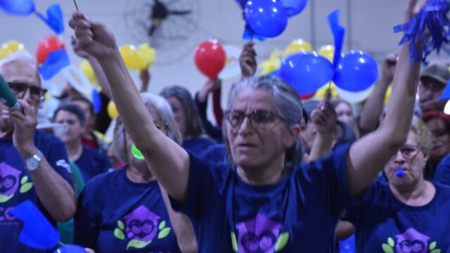 Idosos com camisetas azuis celebram com balões e adereços em evento esportivo em Ponta Grossa