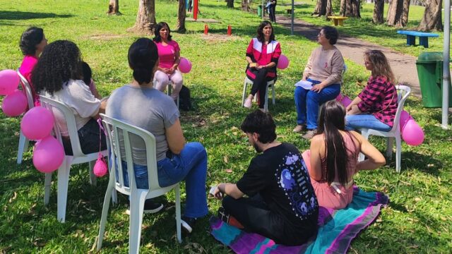 Mulheres sentadas em roda em gramado de parque durante ação do Outubro Rosa
