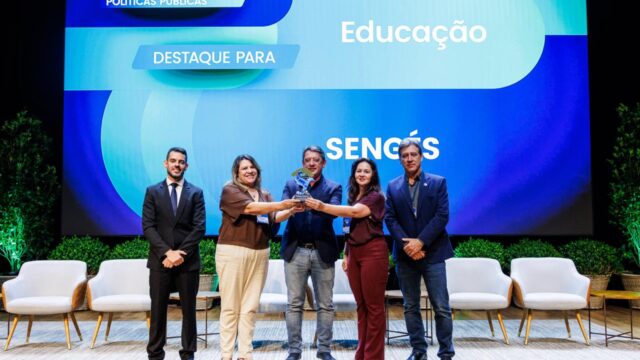 Cinco gestores públicos posando no palco com troféu e telão ao fundo no evento ProGov