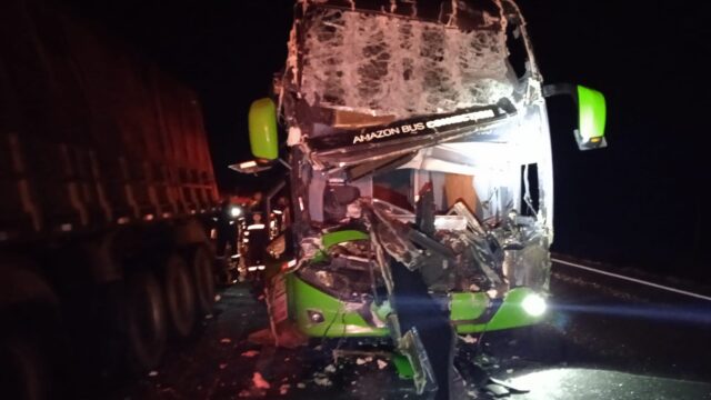 Frente de ônibus verde destruída após batida em rodovia à noite