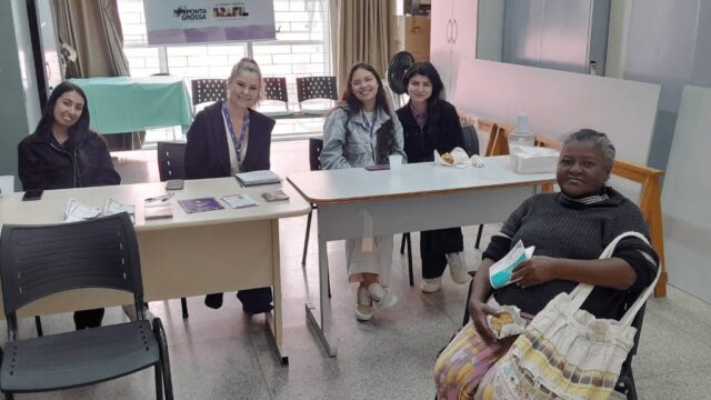 Mulheres sentadas em mesas de atendimento durante ação do CRMB Itinerante no CRAS Coronel Cláudio em Ponta Grossa