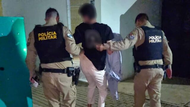 Dois policiais militares conduzem homem algemado na Central de Flagrantes em Cascavel