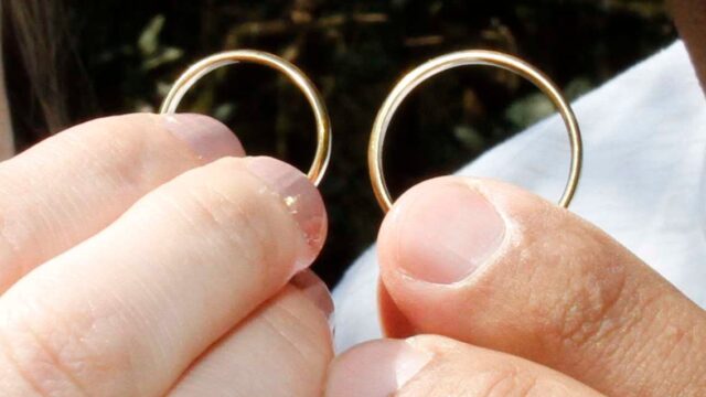 Duas pessoas segurando e exibindo alianças de casamento em close-up