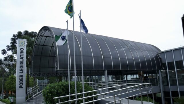 Fachada do prédio da Câmara Municipal de Ponta Grossa com placas e bandeiras ao fundo