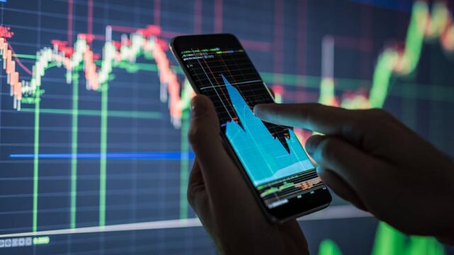 Mão segura smartphone exibindo gráfico de investimentos em tela com dados financeiros