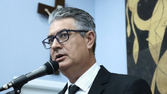 Homem de terno preto, camisa xadrez e óculos discursa em microfone na Câmara Municipal de Ponta Grossa