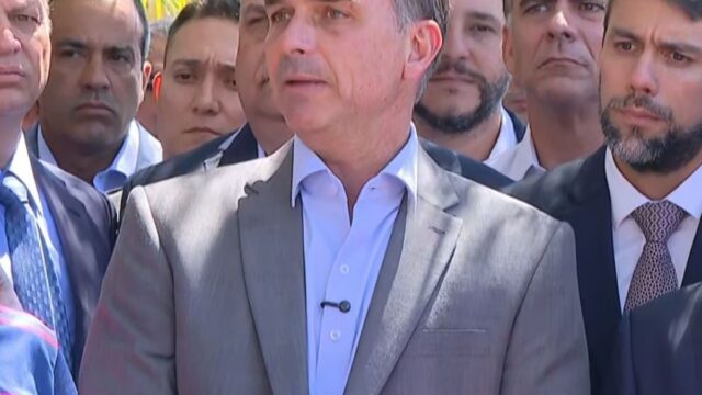 Flávio Bolsonaro discursa cercado por parlamentares e microfones de imprensa