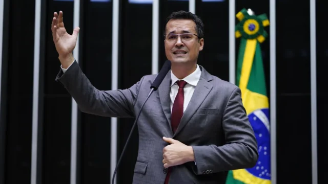 Deltan Dallagnol veste terno cinza e gravata vermelha gesticulando no plenário