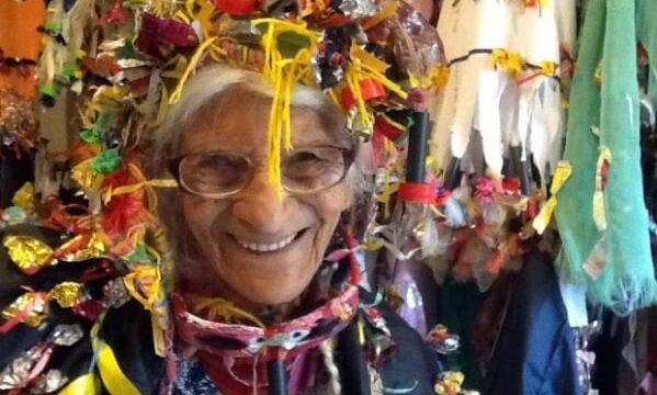 Efigênia Rolim usando chapéu e vestimentas coloridas feitas de materiais reciclados