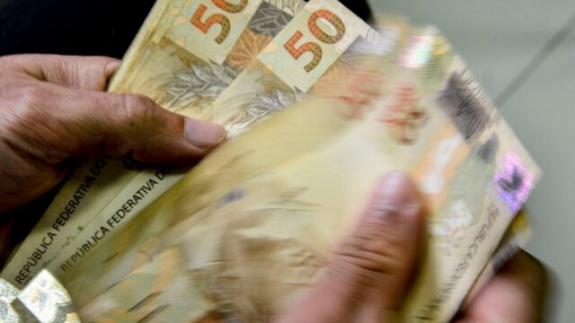 Mãos segurando e contando várias notas de cinquenta reais do real brasileiro