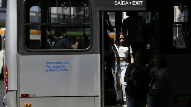 Passageiros descem pela porta de um ônibus urbano com letreiro de saída