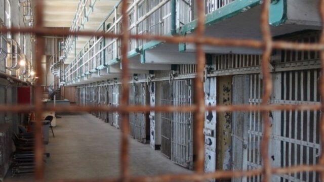 Corredor interno de presídio com grades metálicas e celas enfileiradas
