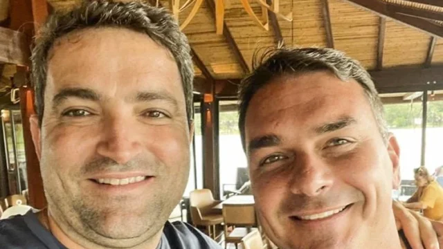 O senador Flávio Bolsonaro ao lado do advogado Willer Tomaz sorrindo em ambiente interno